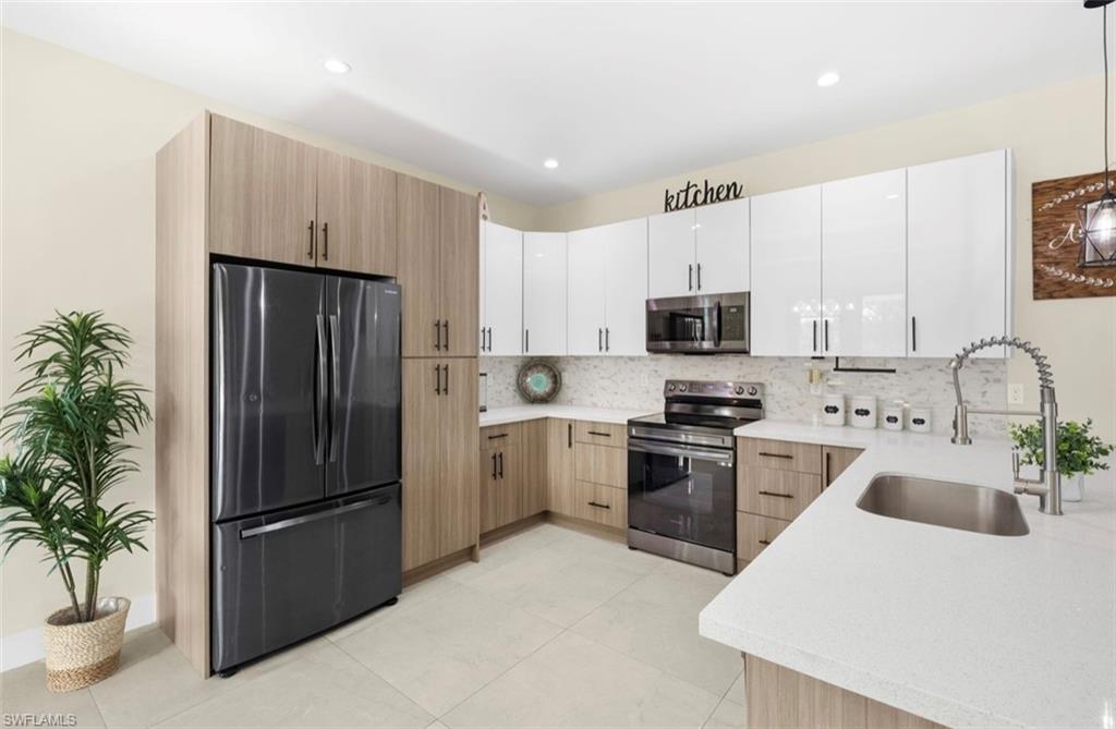 Modern kitchen featuring two-tone cabinetry, stainless steel appliances, a white quartz countertop, and a white mosaic tile backsplash