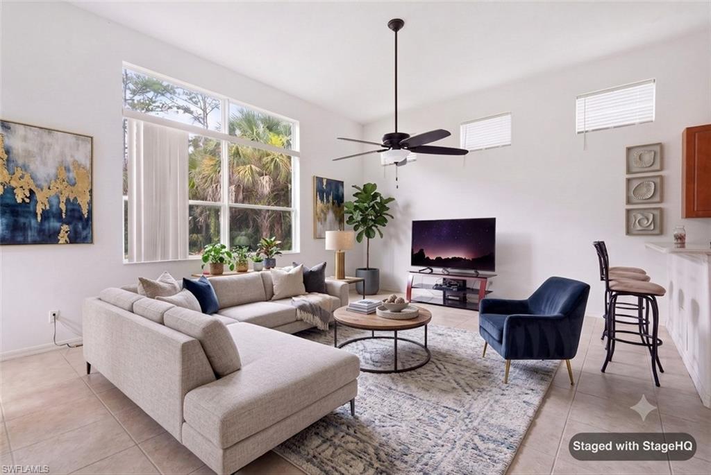Spacious living area featuring large windows, transom windows, a ceiling fan, tiled flooring, and a breakfast bar with seating. Furnishings virtually Staged