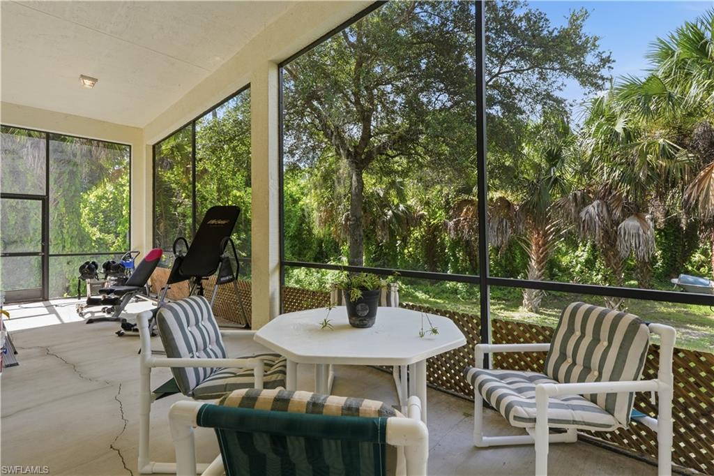 Screened lanai featuring concrete flooring, a textured ceiling, and expansive views of mature trees and tropical foliage