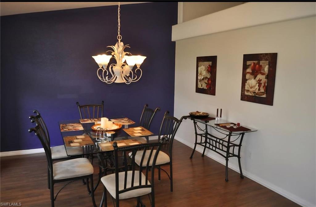 Dining area featuring a prominent chandelier, rich wood-finish flooring, a deep purple accent wall, and a high ceiling