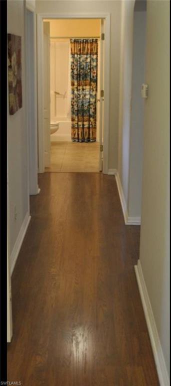 Hallway featuring wood-finish flooring, white baseboards, and light-toned walls