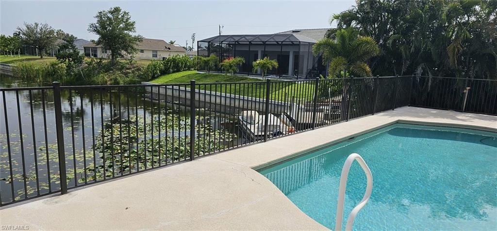 Private swimming pool with a concrete surround, canal frontage with a boat lift, and a black wrought iron fence