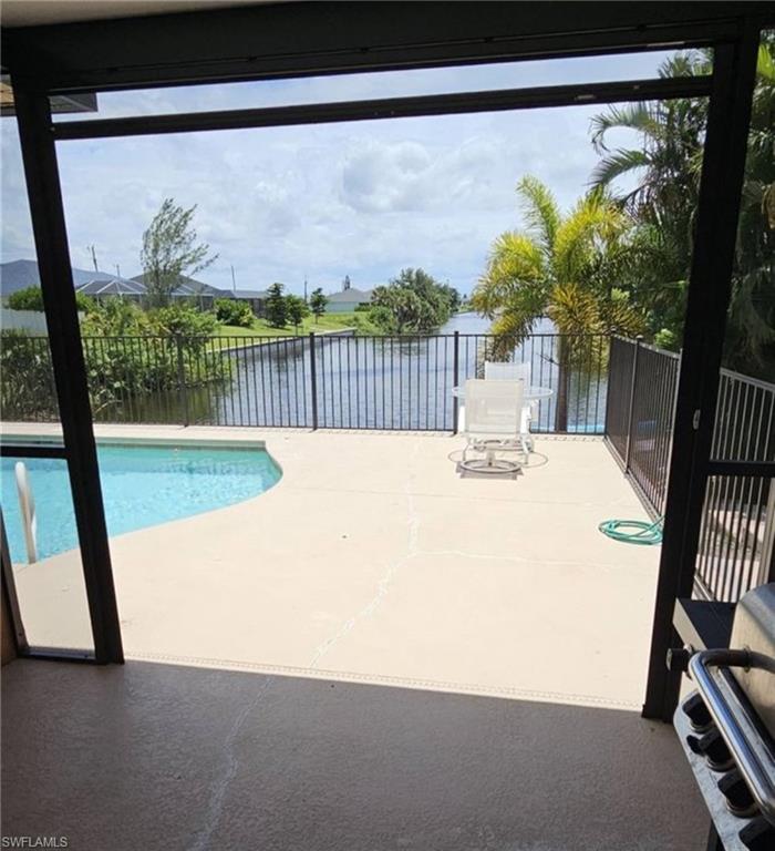Screened patio featuring a curved swimming pool, expansive pool deck, and black metal fencing