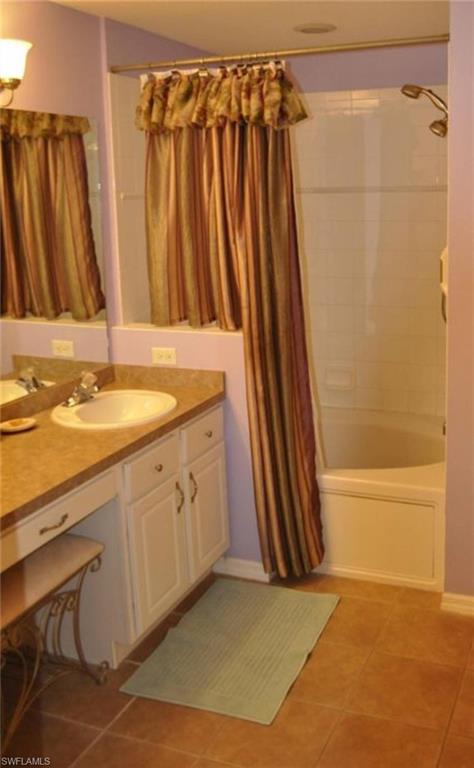 Bathroom featuring a built-in corner tub with tiled surround, a vanity with an integrated sink and base cabinetry, a separate dressing table area, and tile flooring