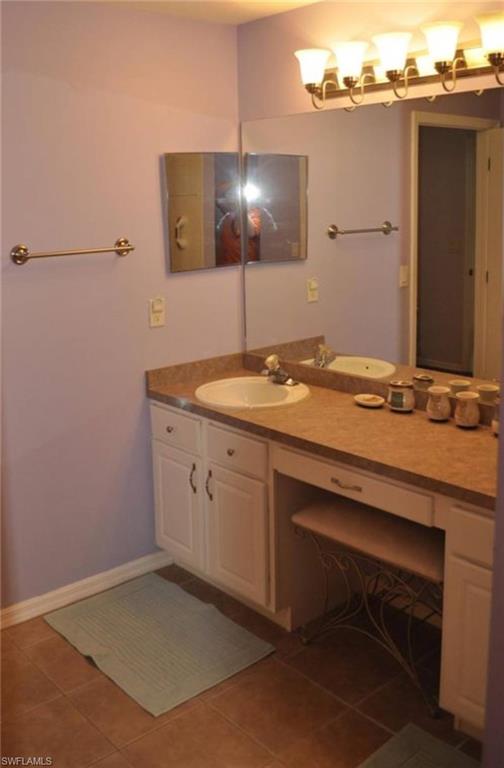 Dual vanity with integrated sinks and countertop, accompanied by white cabinetry and a dedicated vanity seating area
