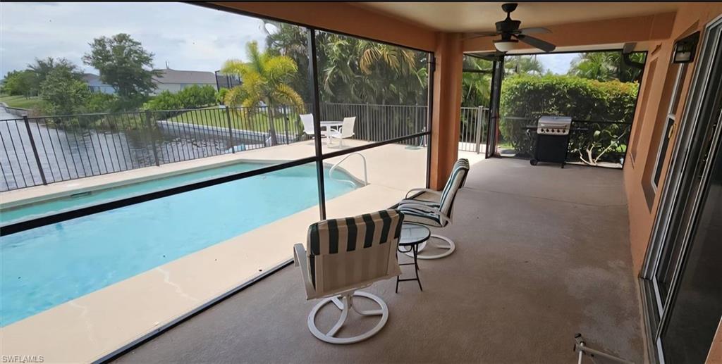 Screened lanai featuring a swimming pool, concrete patio, ceiling fan, and waterfront access with a black metal fence
