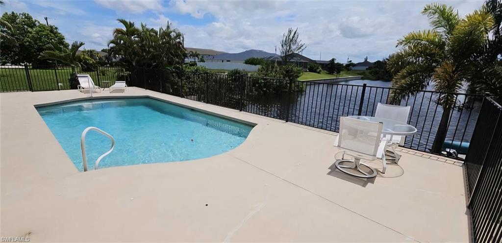 Expansive pool deck featuring a geometric swimming pool, perimeter fencing, and waterfront canal access with a mountain backdrop