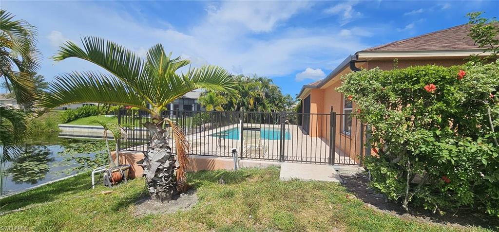 Outdoor pool area featuring a metal fence surround, concrete patio, and mature landscaping