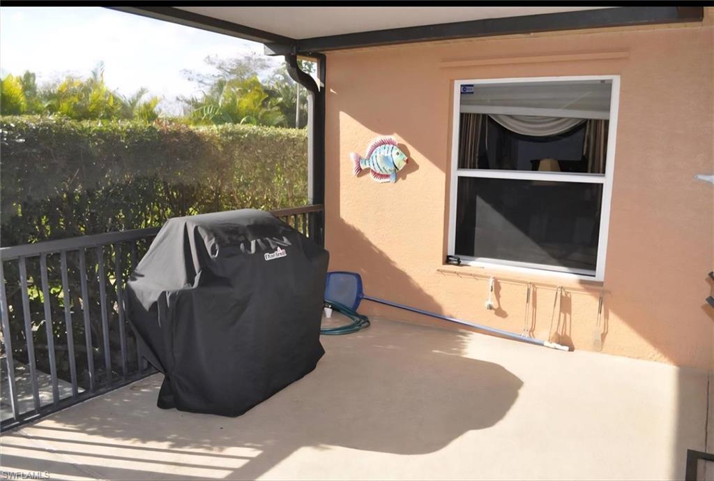 Covered patio with concrete flooring, bordered by a black metal railing and dense hedge