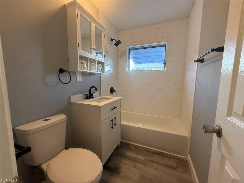 Bathroom featuring a modern vanity with integrated sink, matte black fixtures, white subway tile shower surround, and wood-finish flooring