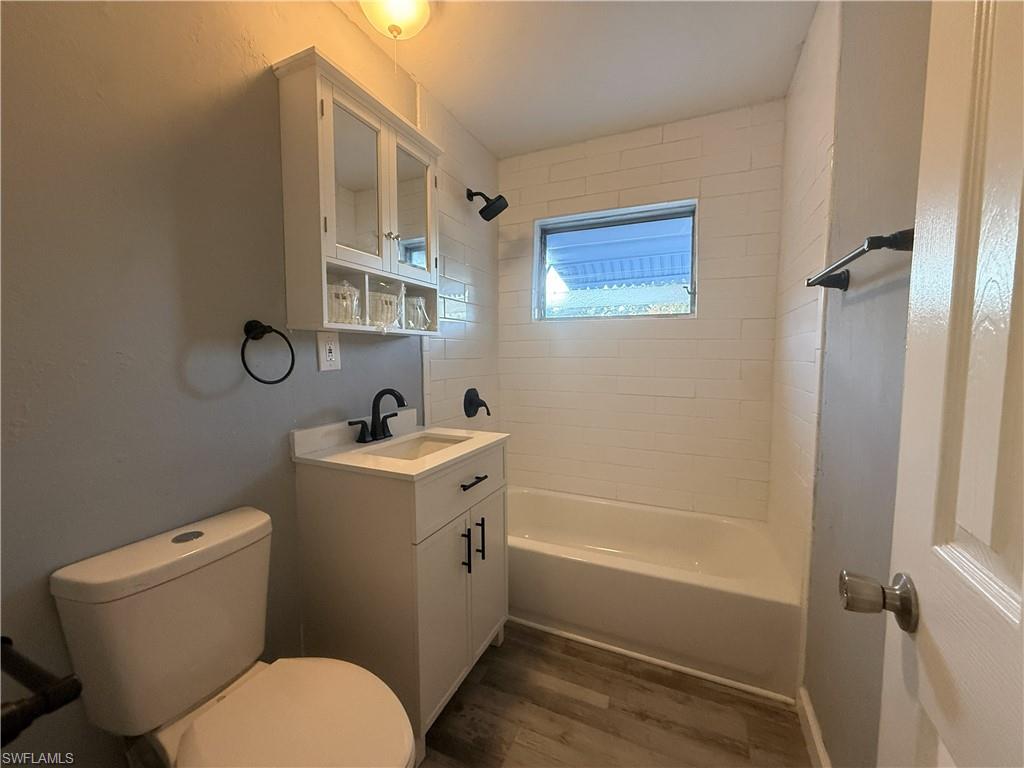 Bathroom featuring a white vanity with a single basin sink, matte black fixtures, a white bathtub, and wood-finish flooring