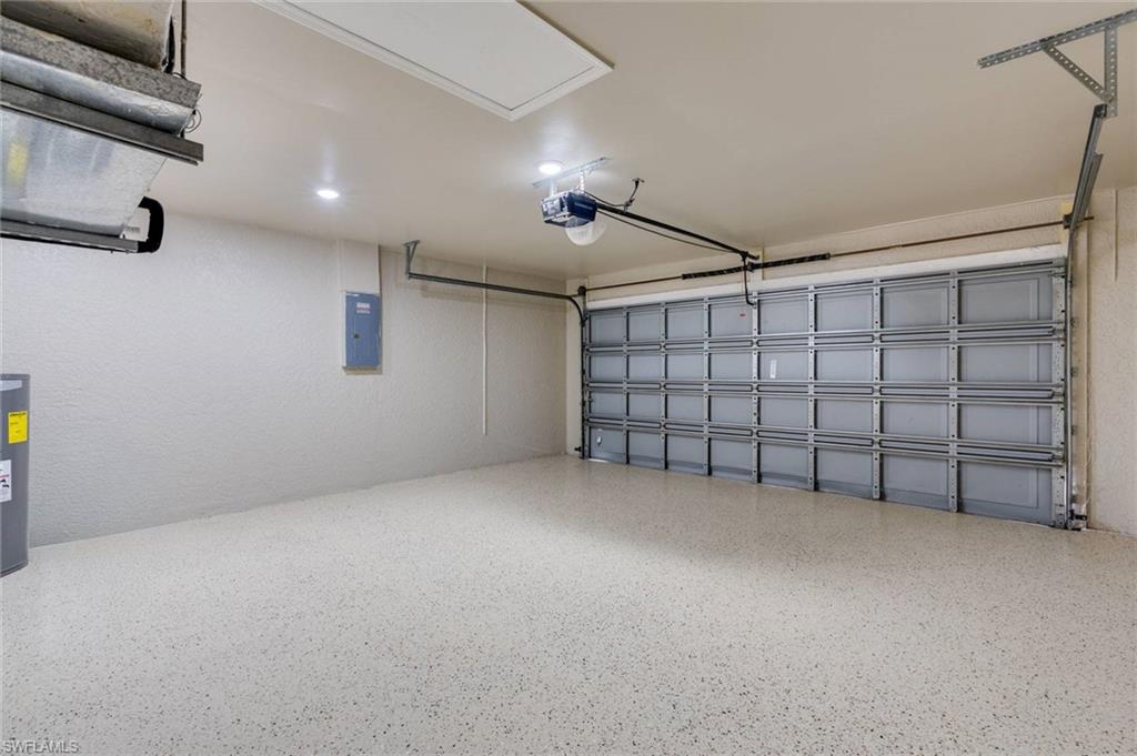 Spacious two-car garage featuring epoxy-coated concrete flooring, overhead sectional door with automatic opener, integrated ceiling-mounted lighting, and ample storage potential with wall-mounted organizational systems