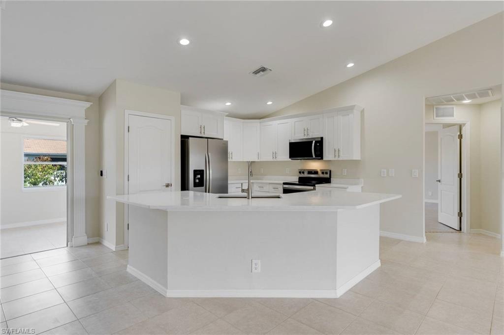 Open-concept kitchen featuring a large island with white cabinetry, stainless steel appliances including a refrigerator with ice and water dispensers, recessed lighting throughout, and tile flooring that extends into the adjoining living spaces