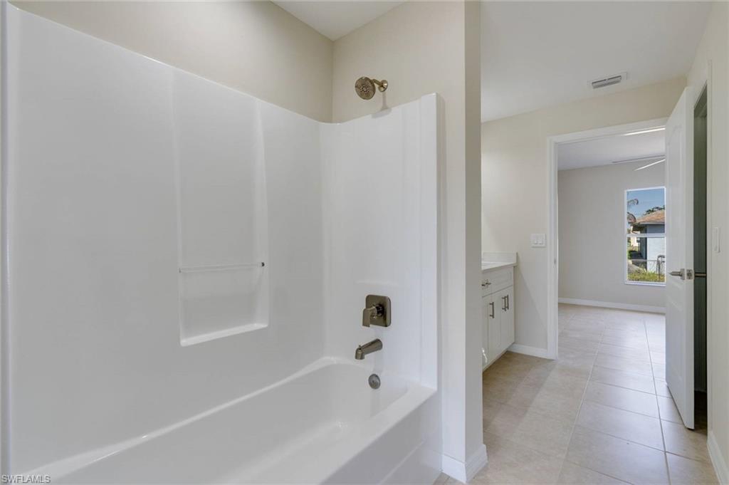 Spa-inspired primary bathroom featuring a white acrylic sobatub with integrated surround, chrome fixtures, tile flooring, and ample natural lighting from recessed ceiling elements