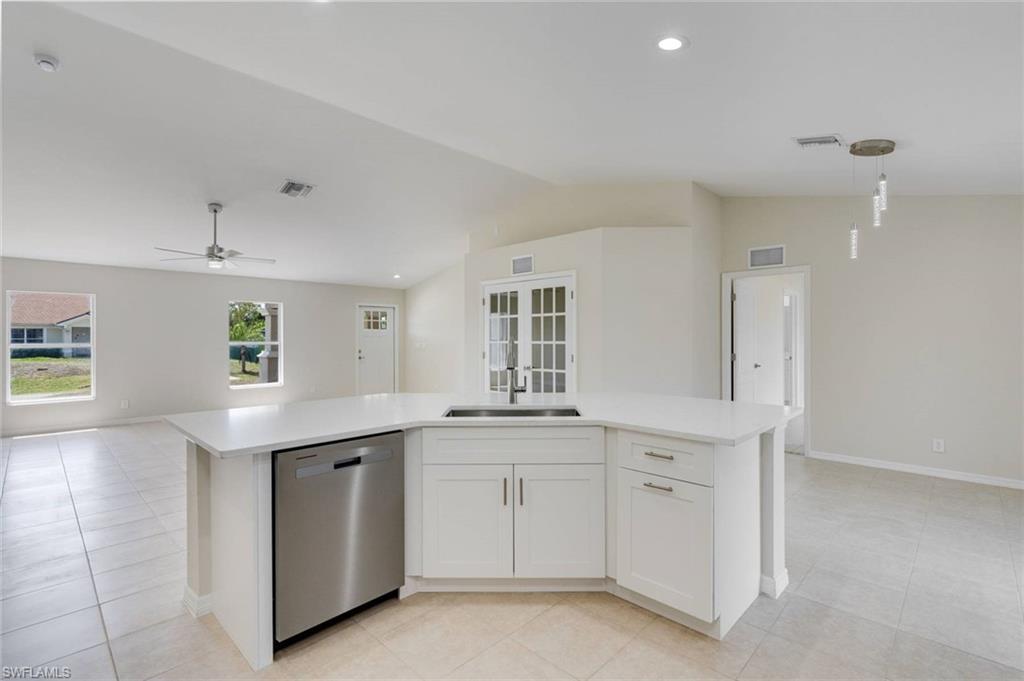 Modern kitchen featuring white cabinetry with brushed nickel hardware, stainless steel dishwasher, light-filled layout with recessed ceiling lighting, and tile flooring throughout the open-concept space
