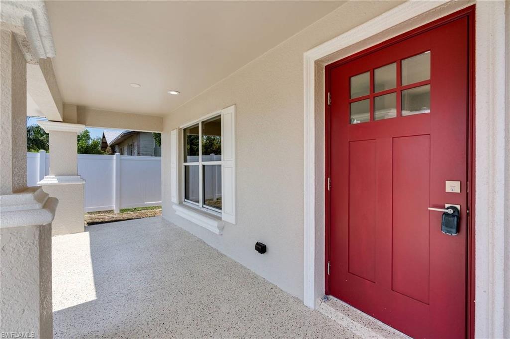 Welcoming covered entryway with polished concrete flooring, recessed lighting, and a striking red entry door featuring six-panel design with frosted glass inserts and electronic keypad entry