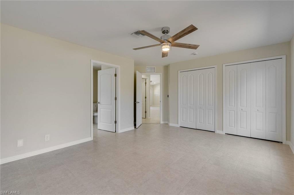 Spacious primary suite showcasing neutral carpeting, ceiling fan with integrated lighting, dual walk-in closets with white panel doors, and multiple entry points including ensuite bathroom access