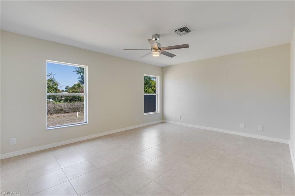 Spacious room flooded with natural light from dual windows, featuring tile flooring throughout, a ceiling fan with integrated lighting, and fresh neutral walls ideal for personalization