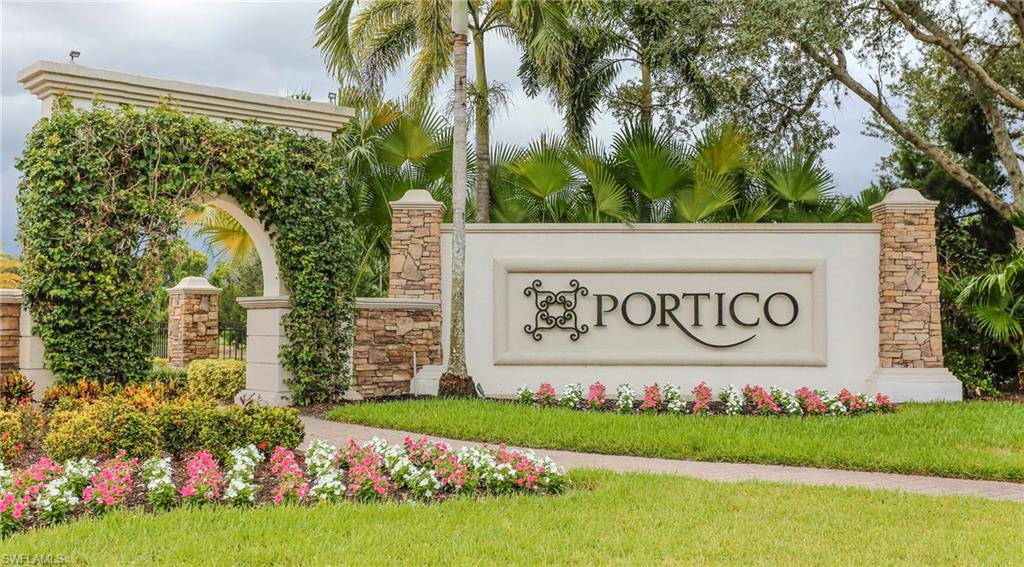 Stone and stucco entry sign with wrought iron detailing, flanked by a manicured landscape featuring an ivy-covered archway and vibrant floral plantings