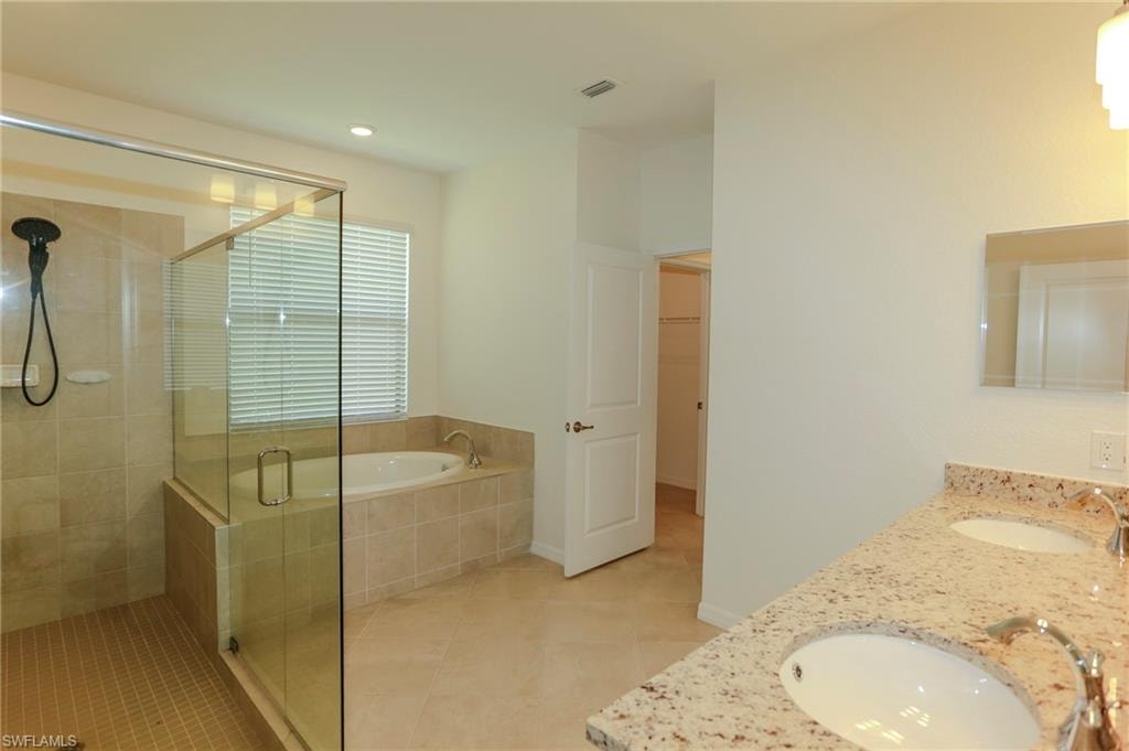 Tile flooring, glass-enclosed shower, built-in soaking tub, dual vanity with undermount sinks, and stone countertop