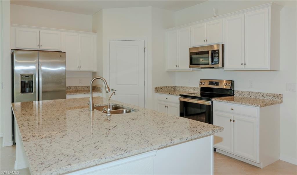 Kitchen featuring white cabinetry, light-toned granite countertops, stainless steel appliances, and a central island with an integrated sink