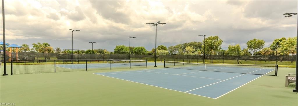 Two hard-surface tennis courts featuring perimeter fencing, multiple overhead lighting fixtures, and a green court surround