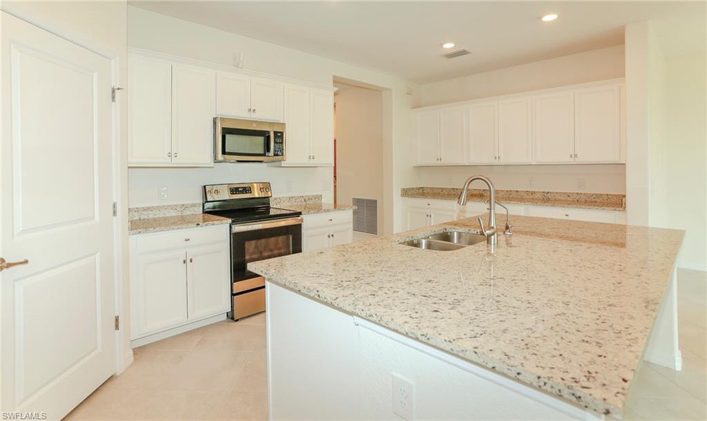 Kitchen featuring white cabinetry, light-toned countertops, stainless steel appliances, a center island with an undermount sink, and recessed lighting
