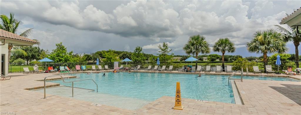 Community swimming pool with a surrounding paved deck, multiple lounge chairs, and mature palm trees