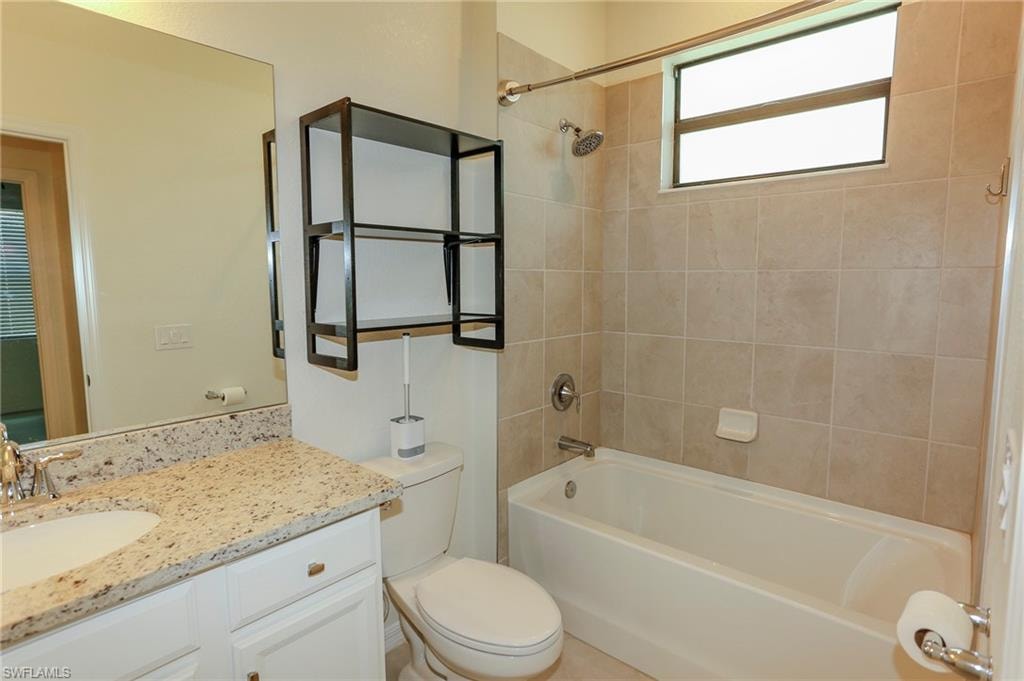 Bathroom featuring a white vanity with a granite-style countertop, undermount sink, large wall mirror, and a shower/tub combination with tiled surround