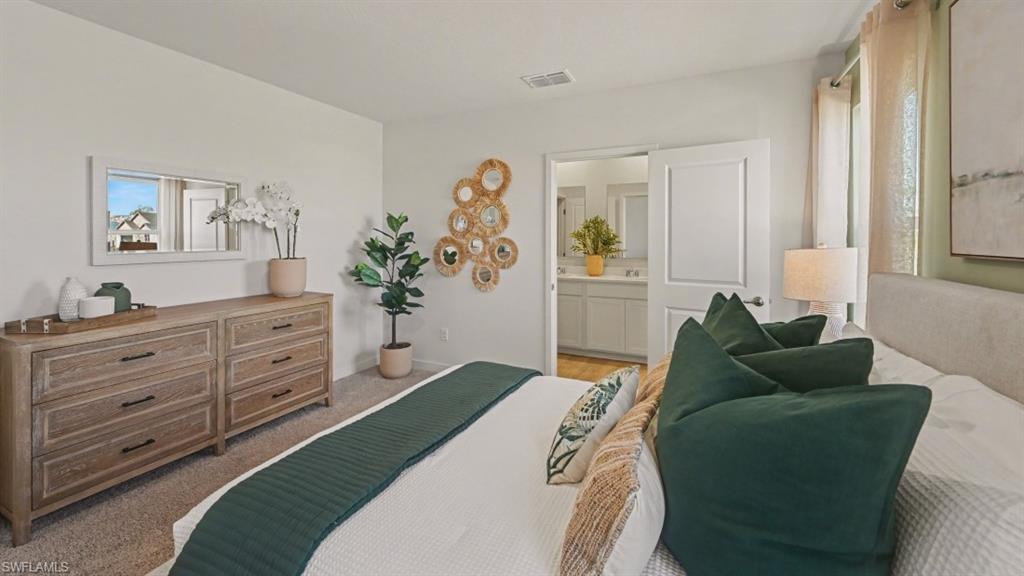 Carpeted bedroom featuring a light-colored wall, a white interior door, and an open doorway revealing a bathroom with a double vanity