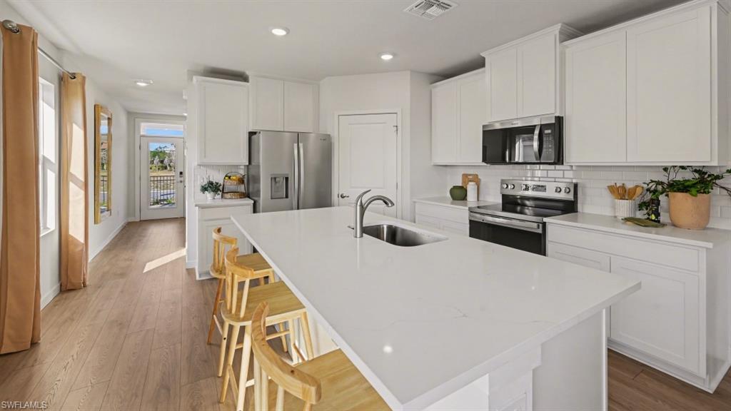 Modern kitchen featuring a large central island with an undermount sink, white cabinetry, stainless steel appliances, white subway tile backsplash, and wood-finish flooring
