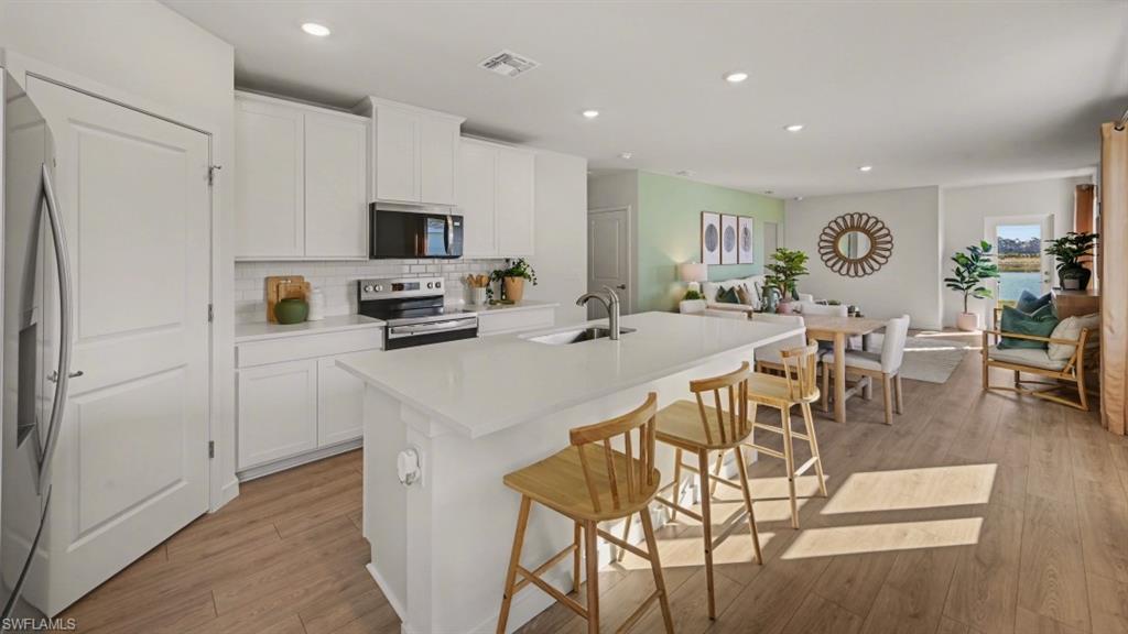 Open-concept living area featuring a kitchen with a large island, white cabinetry, and stainless steel appliances