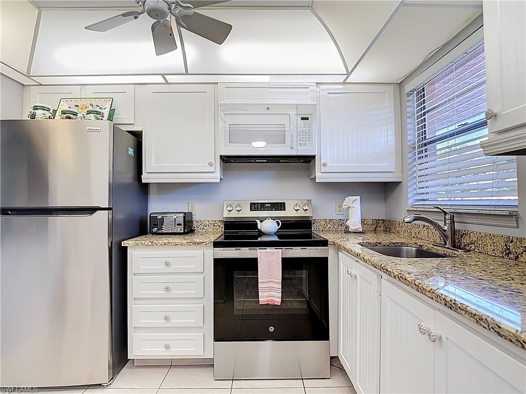 Kitchen featuring appliances with stainless steel finishes, white cabinets, light stone countertops, light tile patterned floors, and a ceiling fan