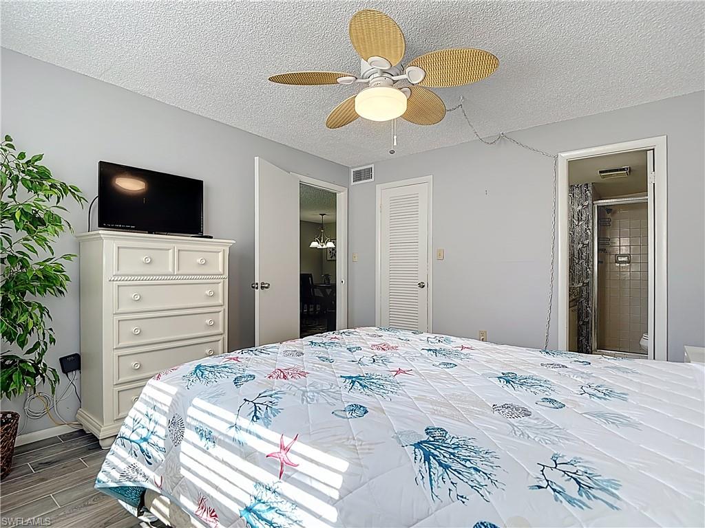 Bedroom with a textured ceiling, wood tiled floors, ceiling fan, and connected bathroom
