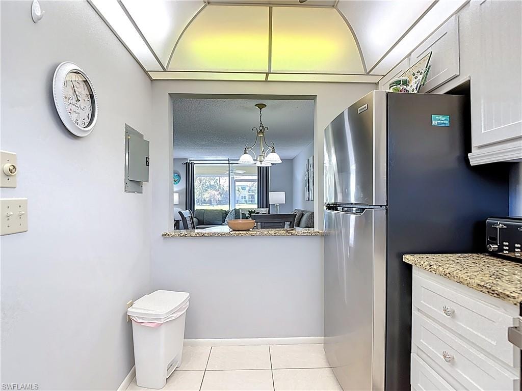 Kitchen featuring light stone counters, light tile patterned floors, freestanding refrigerator, white cabinets, and a chandelier