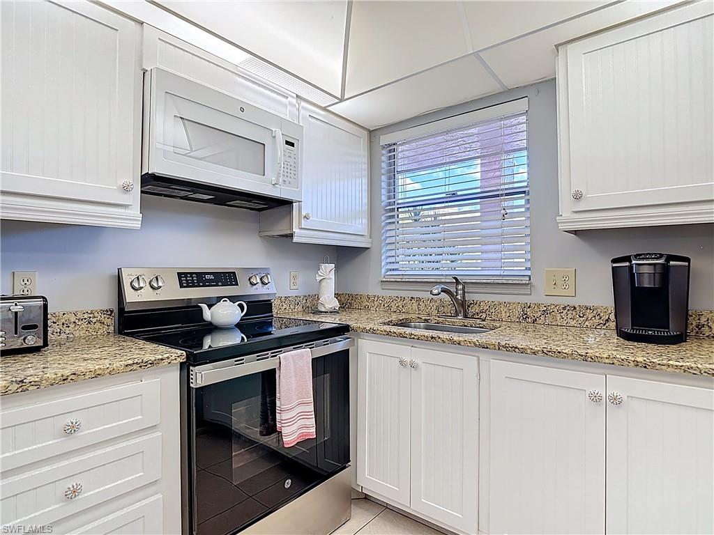 Kitchen with stainless steel electric stove, white cabinets, white microwave, light stone countertops, and light tile patterned flooring