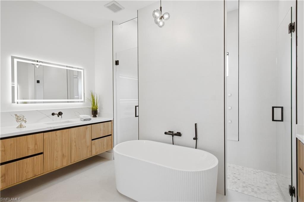 Spa-inspired primary bathroom features a freestanding soaking tub framed by dual floating vanities with illuminated mirrors.
