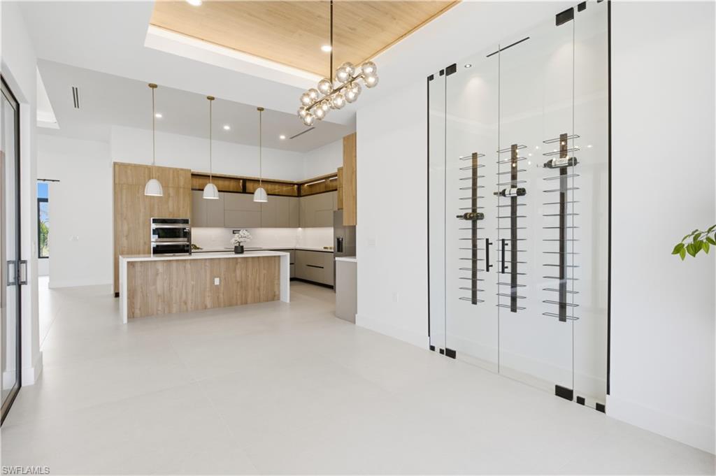 Elegant dining area features a wood-accent tray ceiling, designer chandelier and striking glass-enclosed wine display.