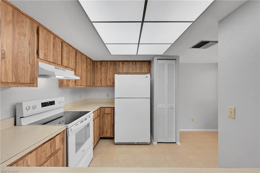 Kitchen with white appliances, light countertops, brown cabinetry, and under cabinet range hood