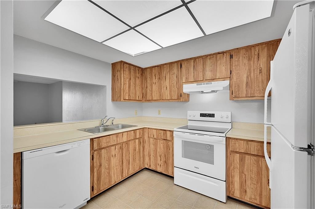 Kitchen featuring white appliances, light countertops, under cabinet range hood, and light tile patterned floors