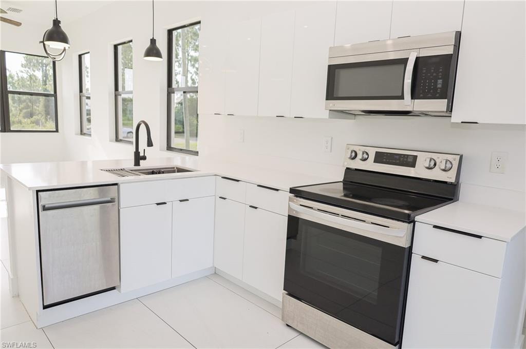 Modern kitchen featuring sleek white cabinetry with minimalist hardware, white countertops, and stainless steel appliances