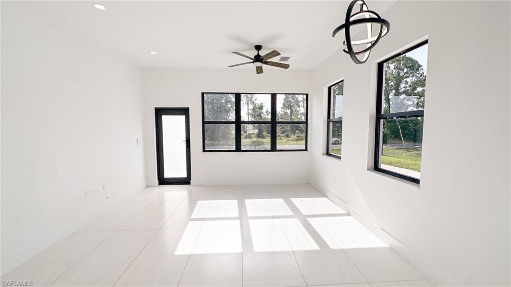 Spacious room featuring white tile flooring, white walls, and multiple large windows with black frames