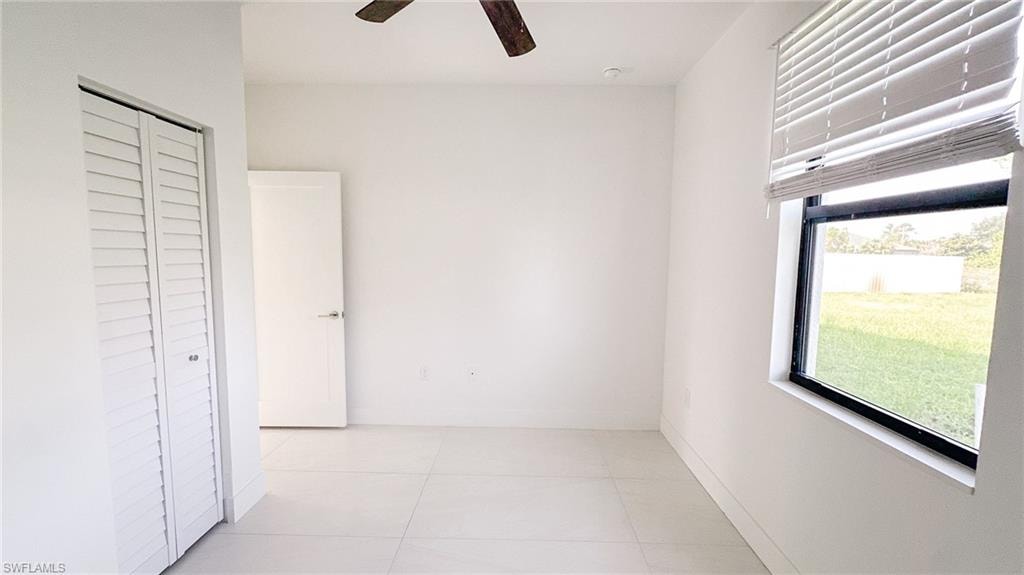 Bright room featuring white walls, large format tile flooring, and a ceiling fan