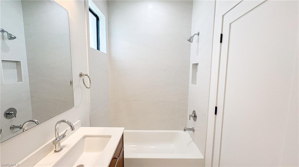 Bathroom featuring a built-in tub with a shower fixture, integrated wall niche, and modern white tiling