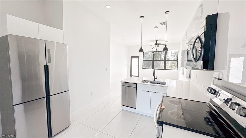 Modern kitchen featuring a stainless steel refrigerator, white cabinetry, integrated dishwasher, and a center island with a farmhouse sink