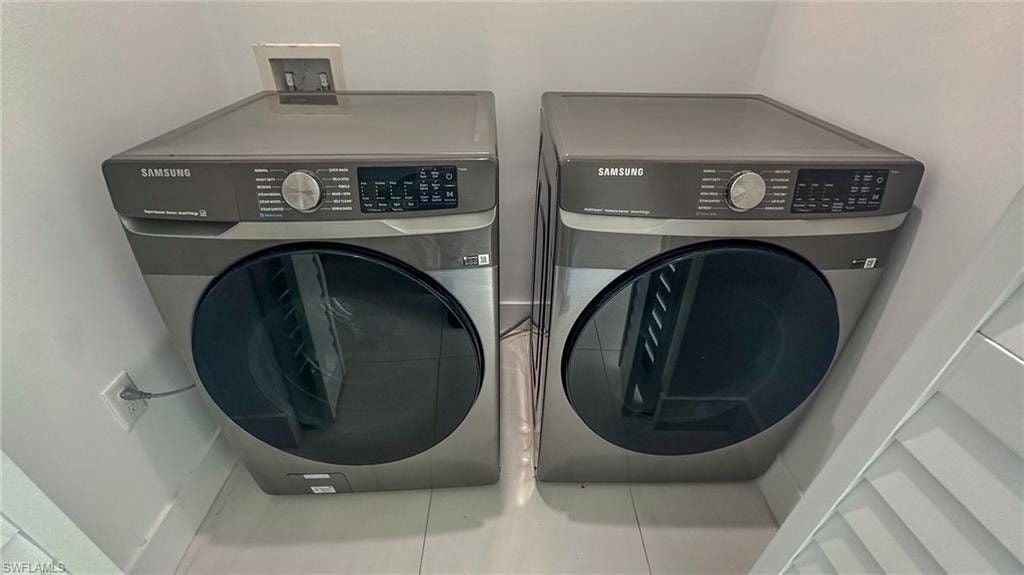 Dedicated laundry area featuring a front-load washer and dryer set, white tile flooring, and clean white walls