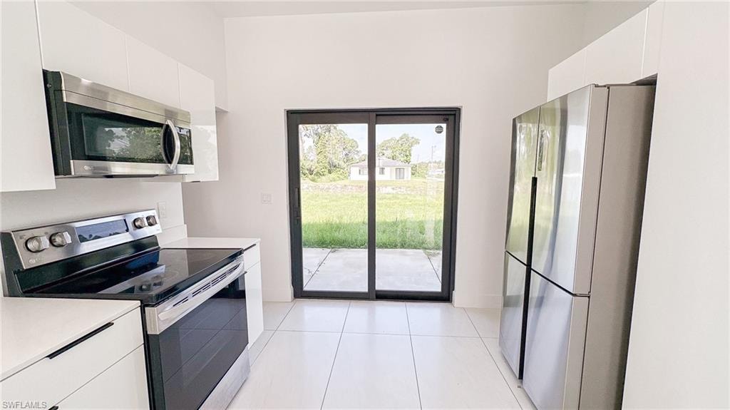 Modern kitchen featuring white cabinetry, stainless steel appliances, white tile flooring, and sliding glass doors to the exterior