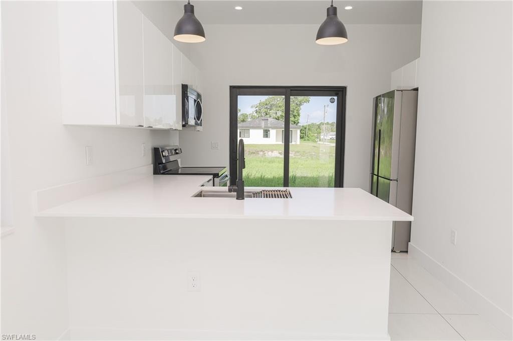 Modern kitchen featuring white cabinetry, light countertops, stainless steel appliances, and a matte black faucet
