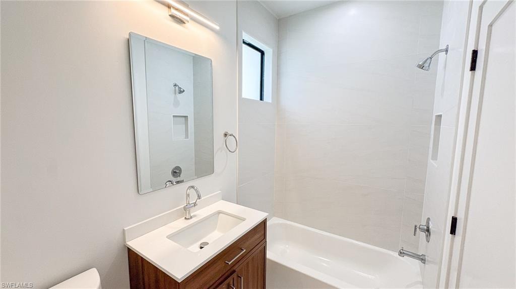 Modern bathroom featuring a wood-finish vanity with a white countertop and undermount sink, a rectangular mirror with integrated lighting, a built-in shower niche, and a white bathtub