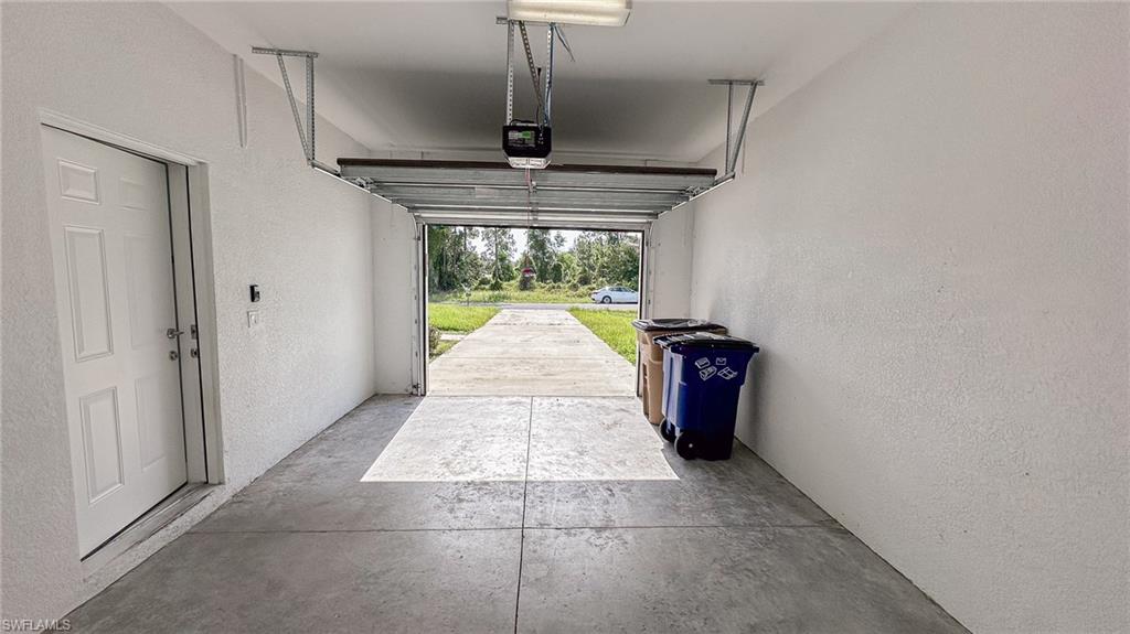 Single-car garage featuring a concrete floor, textured white walls, and an overhead garage door opener